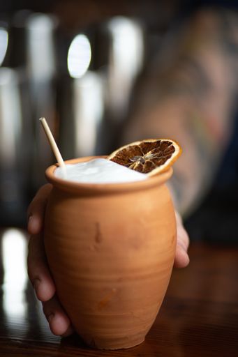 A selective focus shot of a hand holding a drink with a dry slice of lemon in a clay pot