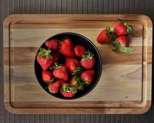 A top view of a bowl with fresh strawberries on a wooden cutting board