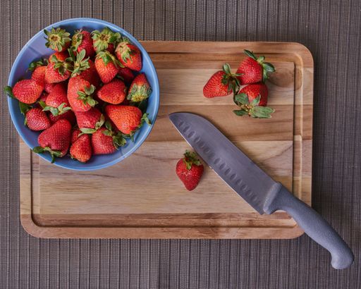 A top view of a bowl of strawberries and a knife on a wooden cutting board