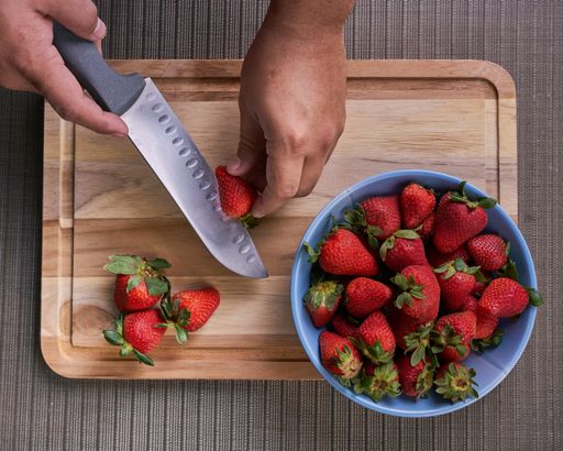 A top view of a person cutting strawberries on a wooden board