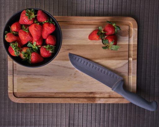 A top view of a bowl of strawberries and a knife on a wooden cutting board