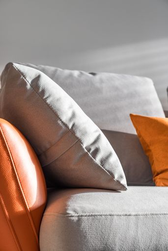 A vertical shot of a modern couch and several grey and orange pillows on it