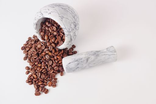 natural roasted coffee beans in a white marble mortar isolated on a white background