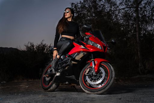 A female model wearing a white outfit and a black helmet poses on a red motorbike in a desert landscape