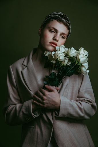 A woman in a gray suit holding a bouquet of white roses.