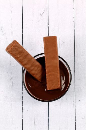 A vertical shot of a bowl of chocolate dip with two bars on a wooden surface