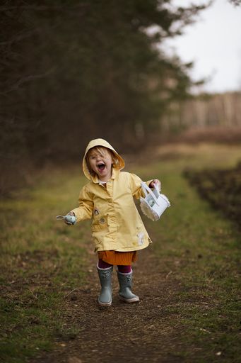 A lovely funny Dutch baby girl in a yellow waterproof coat and boots playing in the countryside field