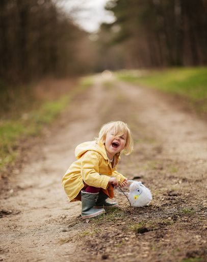 A lovely funny Dutch baby girl in a yellow waterproof coat and boots playing in the countryside field
