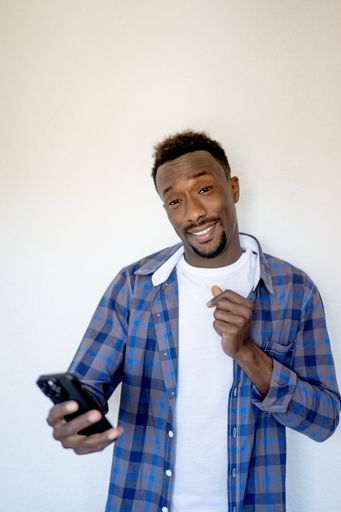 A vertical shot of a cool, handsome Black man posing wearing a blue shirt and holding a smartphone