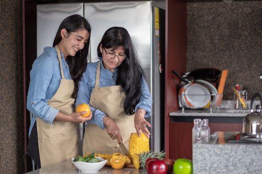 A happy Mexican mother and daughter cutting fruits in the kitchen