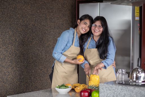 A happy Mexican mother and daughter cutting fruits in the kitchen