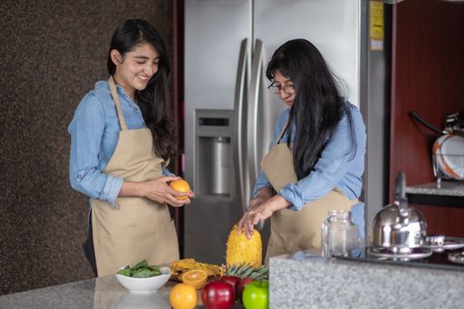 A happy Mexican mother and daughter cutting fruits in the kitchen