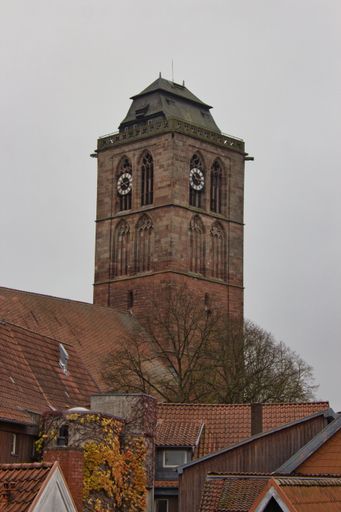 A vertical shot of a clock tower and brown roofs of buildings