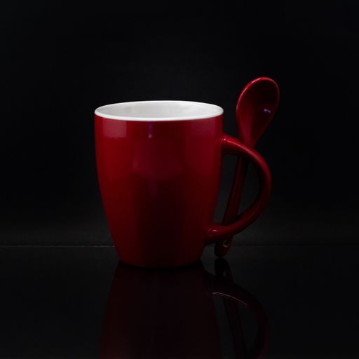 A closeup shot of a red mug with a spoon on a blackbackground