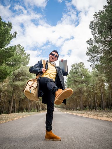A shallow focus of a cool confident man with a bag standing on one leg on the road