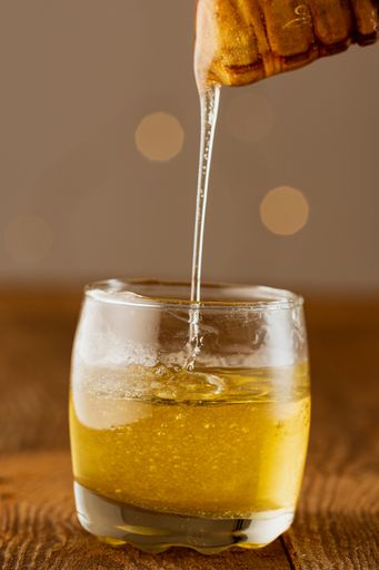 A vertical shot of honey dipping in a transparent glass from a dipper