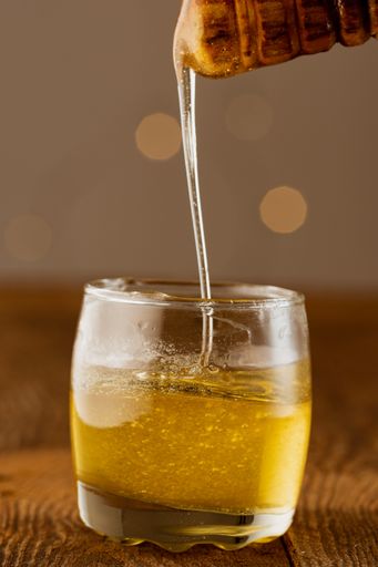 A vertical shot of honey dipping in a transparent glass from a dipper