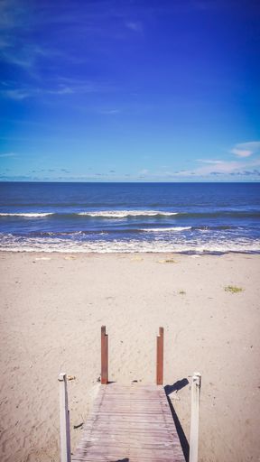 A vertical shot of a boardwalk on the sandy shore of the sea