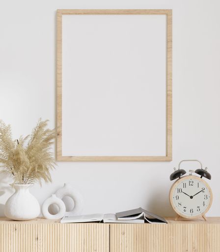 A white framed picture sits atop a shelf that is decorated with lush green plants and a small alarm clock