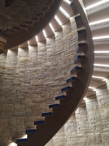 An interior shot of a stone wall featuring a staircase with illuminated spiral steps