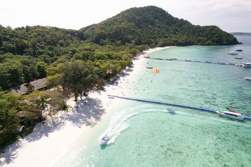 An aerial view of a populated beach with people swimming in the water and resting on the beach