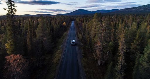 RV in autumn color forest, Aerial drone shot of a Camper van in foliage woods, moving towards Ounastunturit fells, sunny, autumn evening, in Lapland