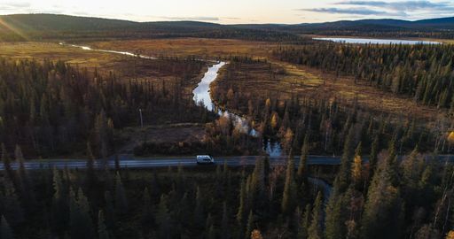 Camper van in a autumn forest in Lappland, aerial drone view of a caravan car, driving in middle of foliage trees, on a sunny fall evening, in Lapland
