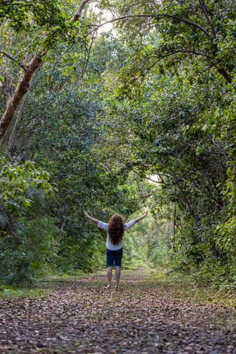 A young woman walking in a natural environment with her arms outstretched in the air