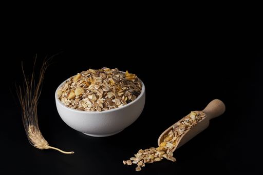 white ceramic bowl with muesli, wooden spoon and ear of wheat isolated on a black background and copy space