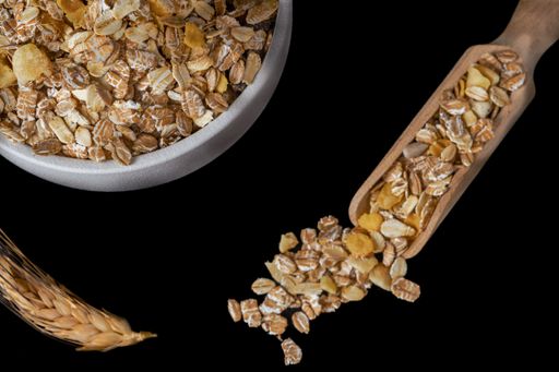 top view of a white ceramic bowl with muesli, wooden spoon and ear of wheat isolated on black background and copy space