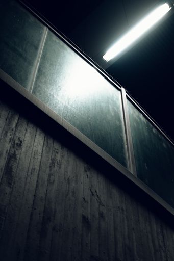 A vertical shot of a wooden wall with windows under the white lamp lights in a dark room