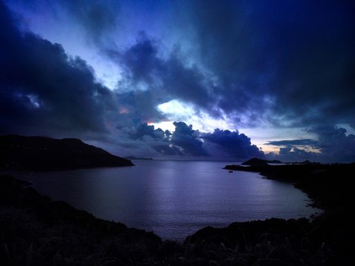 A beautiful blue sky dotted with white, fluffy clouds against a tranquil ocean silhouette