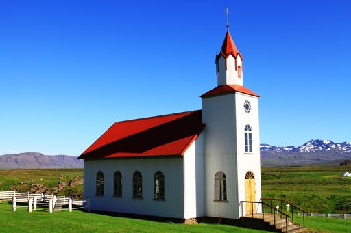 The beautiful Reyniskirkja Church with snowy mountains in the background against a clear blue sky