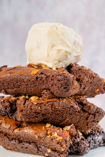 Chocolate brownie with pecan walnuts stacked with vanilla ice cream on top on white pastel backgro. Macro shot.