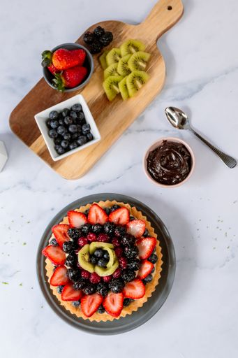 A top view of a delicious fruit tart with ingredients on a marble table