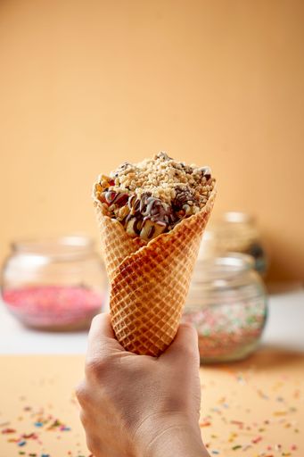 A vertical shot of a hand holding an icecream cone with sprinkles