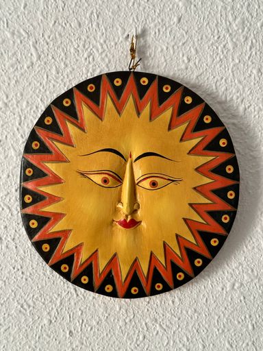 A decorative figure in the shape of a smiling sun hangs on a white wall