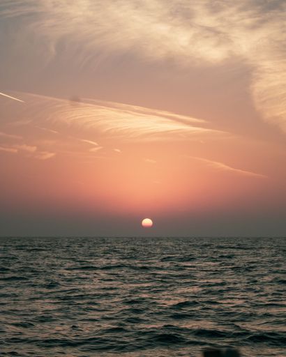 A tranquil scene of a setting sun is captured from the edge of a body of water, creating a serene atmosphere