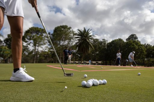 Closeup of white golf balls resting on the lush green grass of a golf course with a male sporting golf attire standing nearby