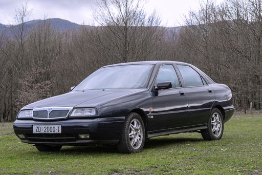 A closeup of a sleek black Lancia Kappa parked on a lush green grassy area