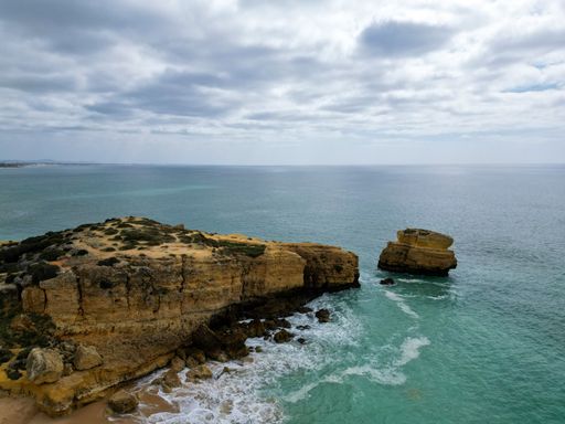 A drone view of a rocky shore surrounded by the sea under a cloudy sky on a gloomy day