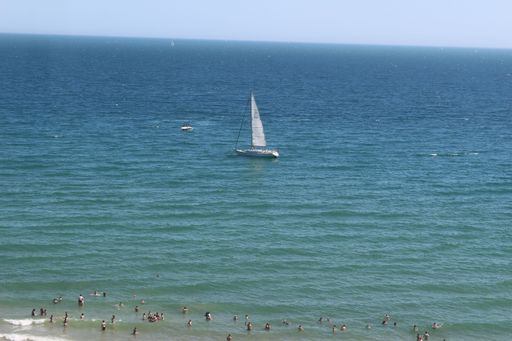 The blue sea with people swimming near the shore and a sailboat in the distance.