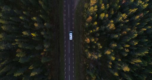 Aerial view above a camper driving on a asphalt road, in arctic tundra, sunny, autumn day, in Lapland, Finland - top down, drone shot