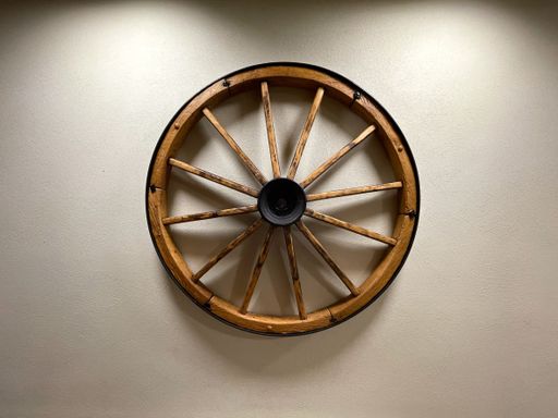An aged wooden wagon wheel is displayed hanging on a crisp white wall, adding an antique and rustic feel to the space
