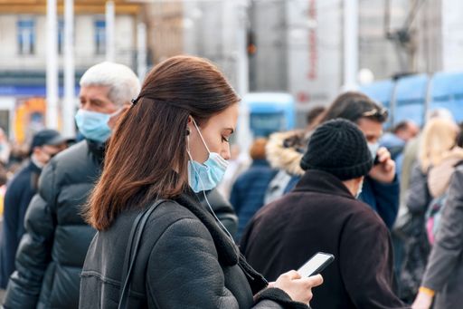 Young woman wearing protective mask, using mobile phone, waiting on tram station. People in city, epidemic, new normal.