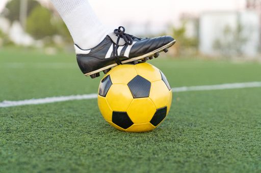 A selective focus shot of a soccer ball and a foot holding it on a field