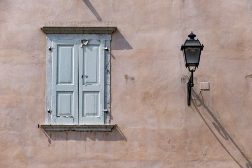 A closeup of an old building wall with blue wooden shutters and vintage street lamp