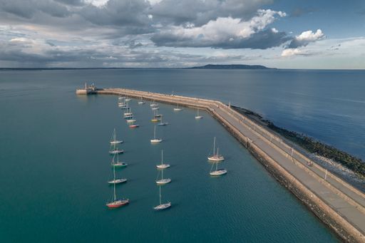An aerial view of a fleet of boats moored along the edge of a dock, reflecting in the still water