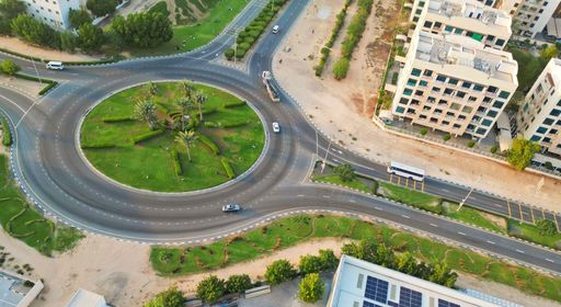An aerial view of a roundabout in a residential area near a town, surrounded by a mixture of buildings and trees