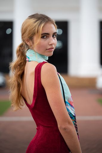 A vertical shot of a young blonde female in a red dress and a scarf posing